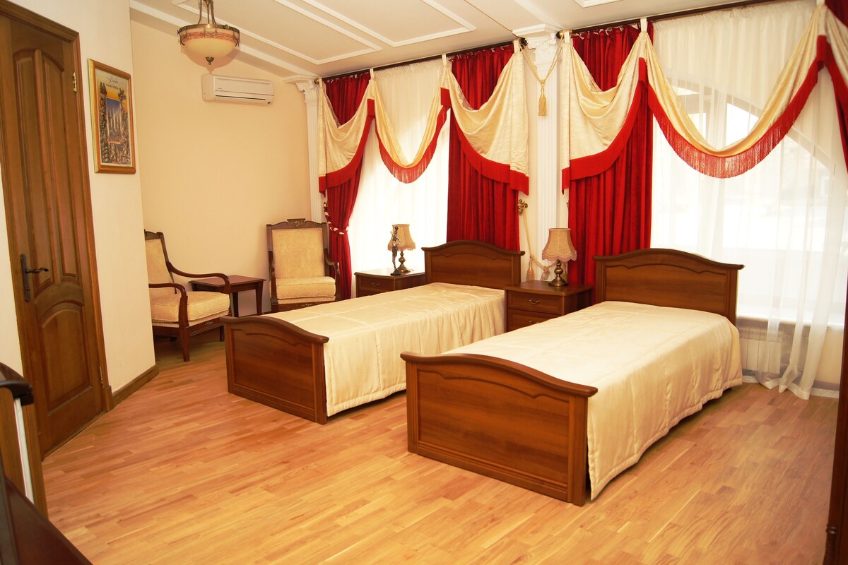 Une chambre d’hôtel avec deux lits en bois, une chaise, une table de chevet et une lampe.