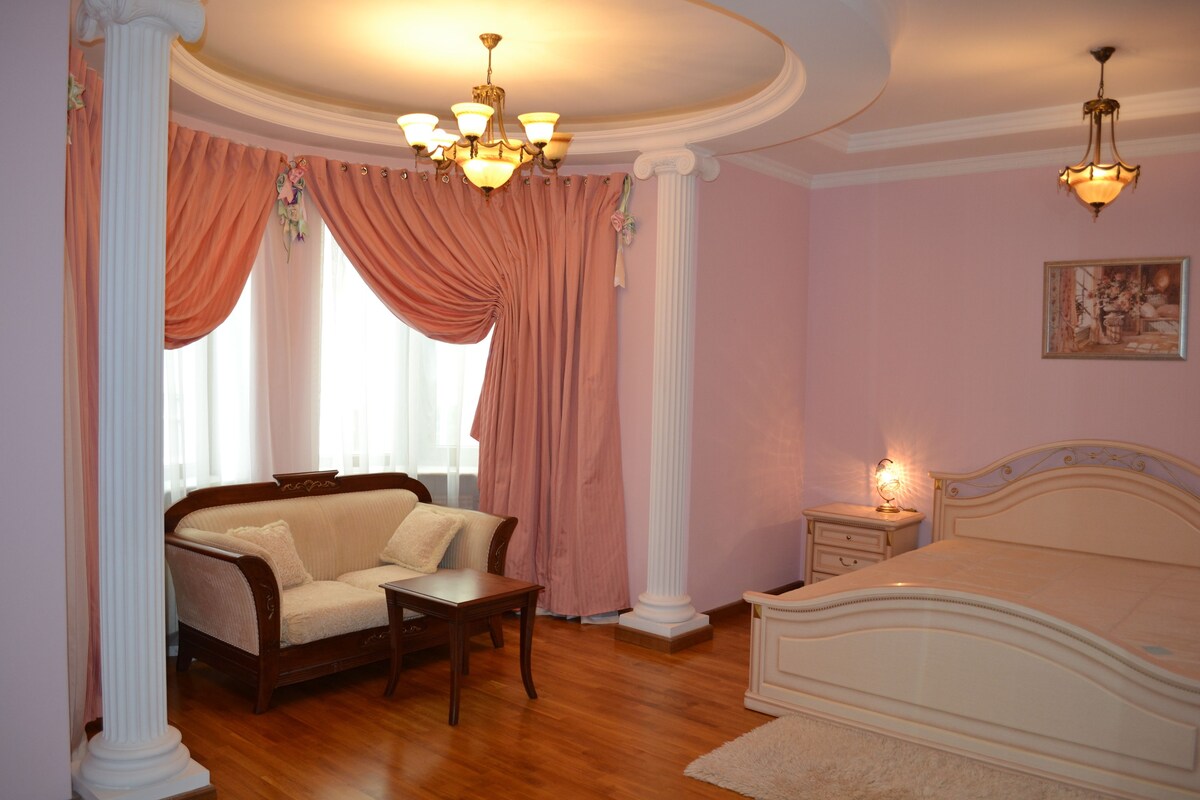 Une chambre à coucher avec un lit, une table de chevet, une chaise, une table et une fenêtre avec des rideaux.