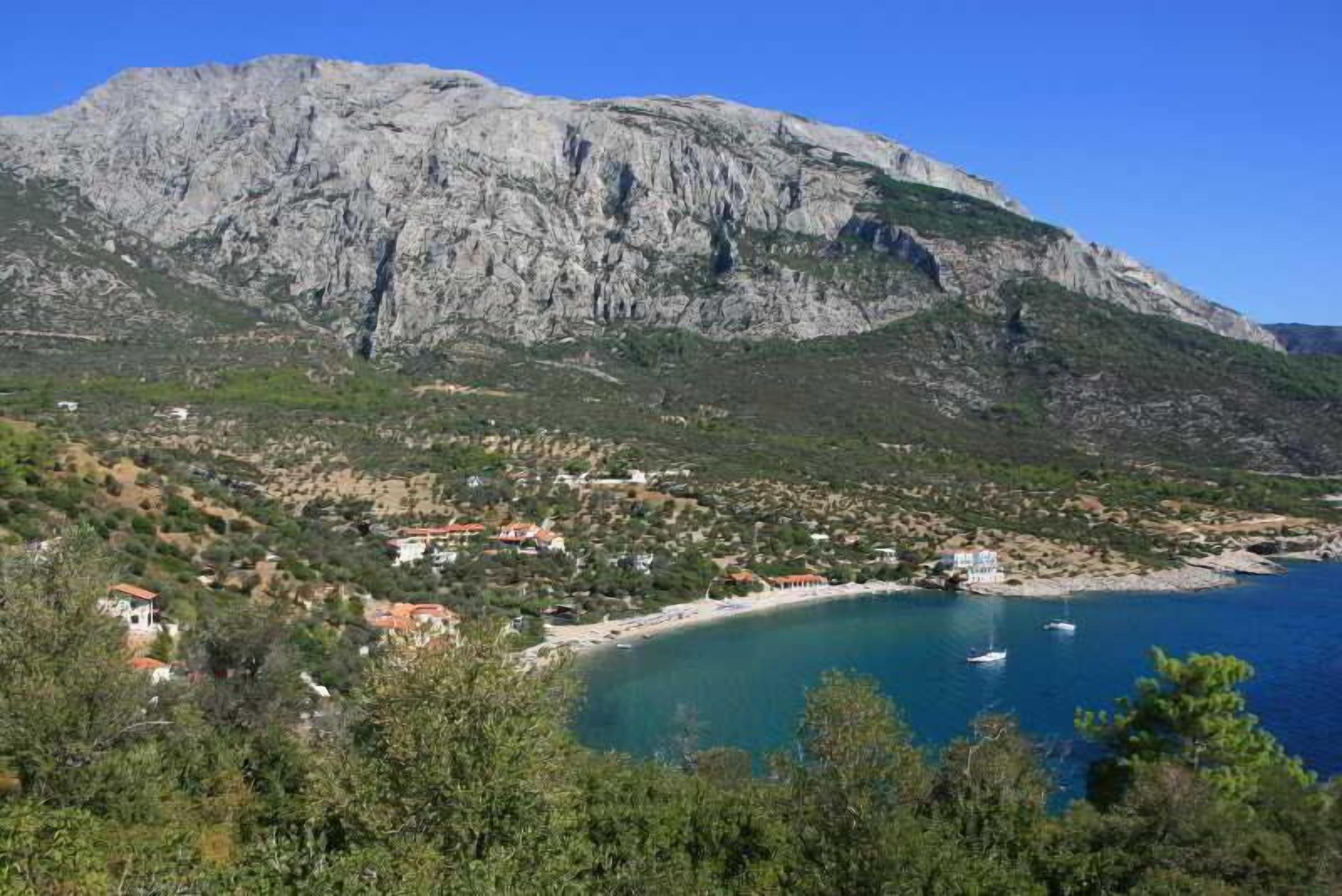 A coastal town with a mountain backdrop, clear blue waters, and scattered buildings.