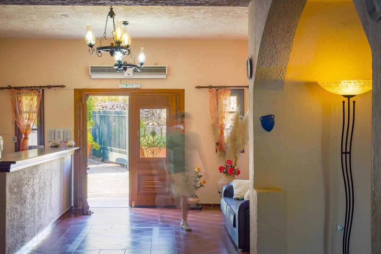 Vestíbulo de hotel con mostrador de recepción, candelabro, una lámpara de pared grande y vistas a un área exterior a través de un acceso.
