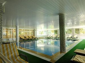 An indoor swimming pool with lounge chairs and a view of greenery outside. - Kırbıyık Resort Hotel (Alanya)
