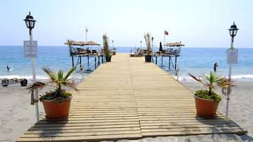 A wooden pier leading to a beach with lounge chairs and potted plants.