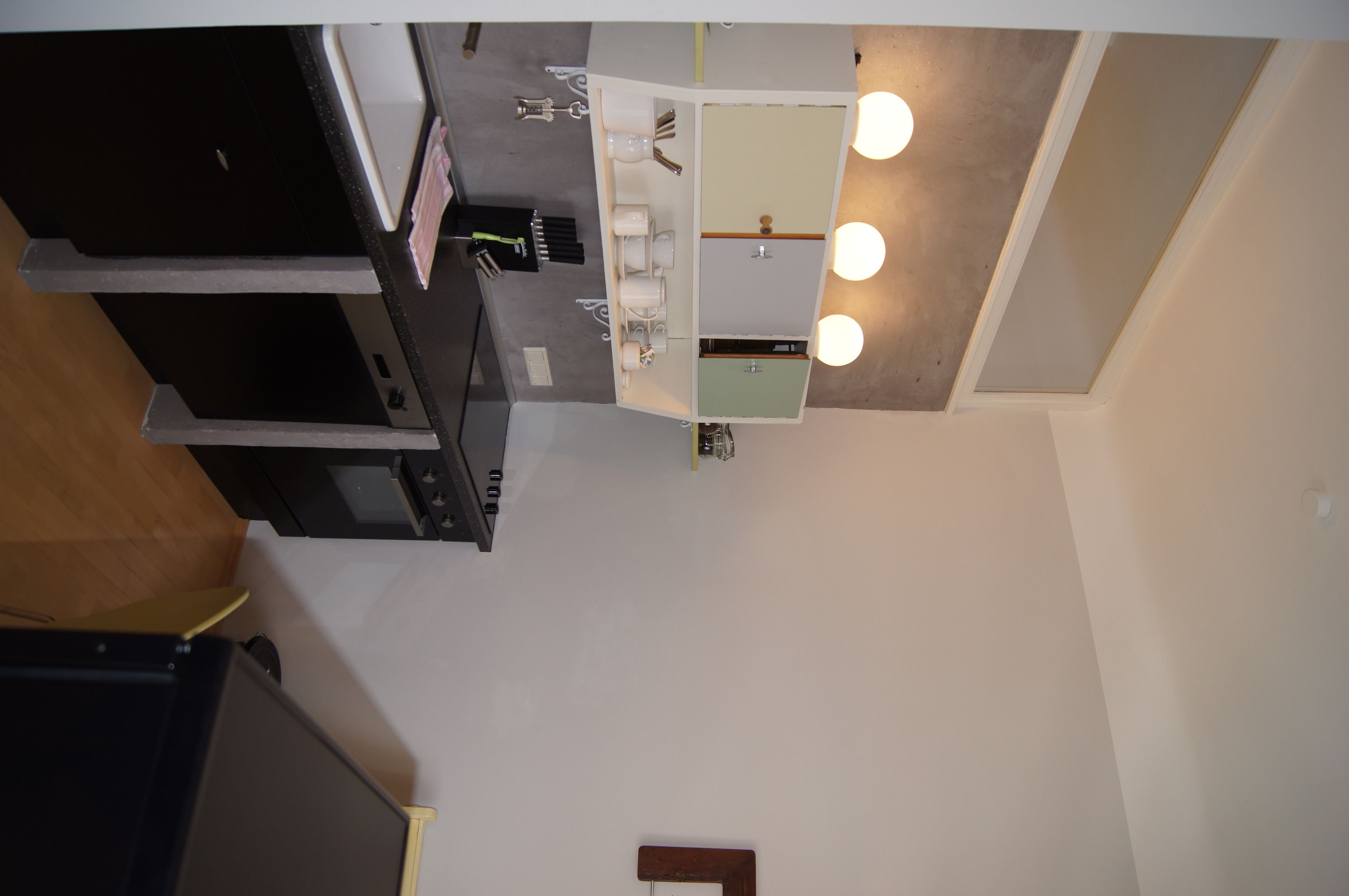 A kitchen with a sink, countertop, and cabinets. There is a mirror above the sink and a ceiling light fixture.