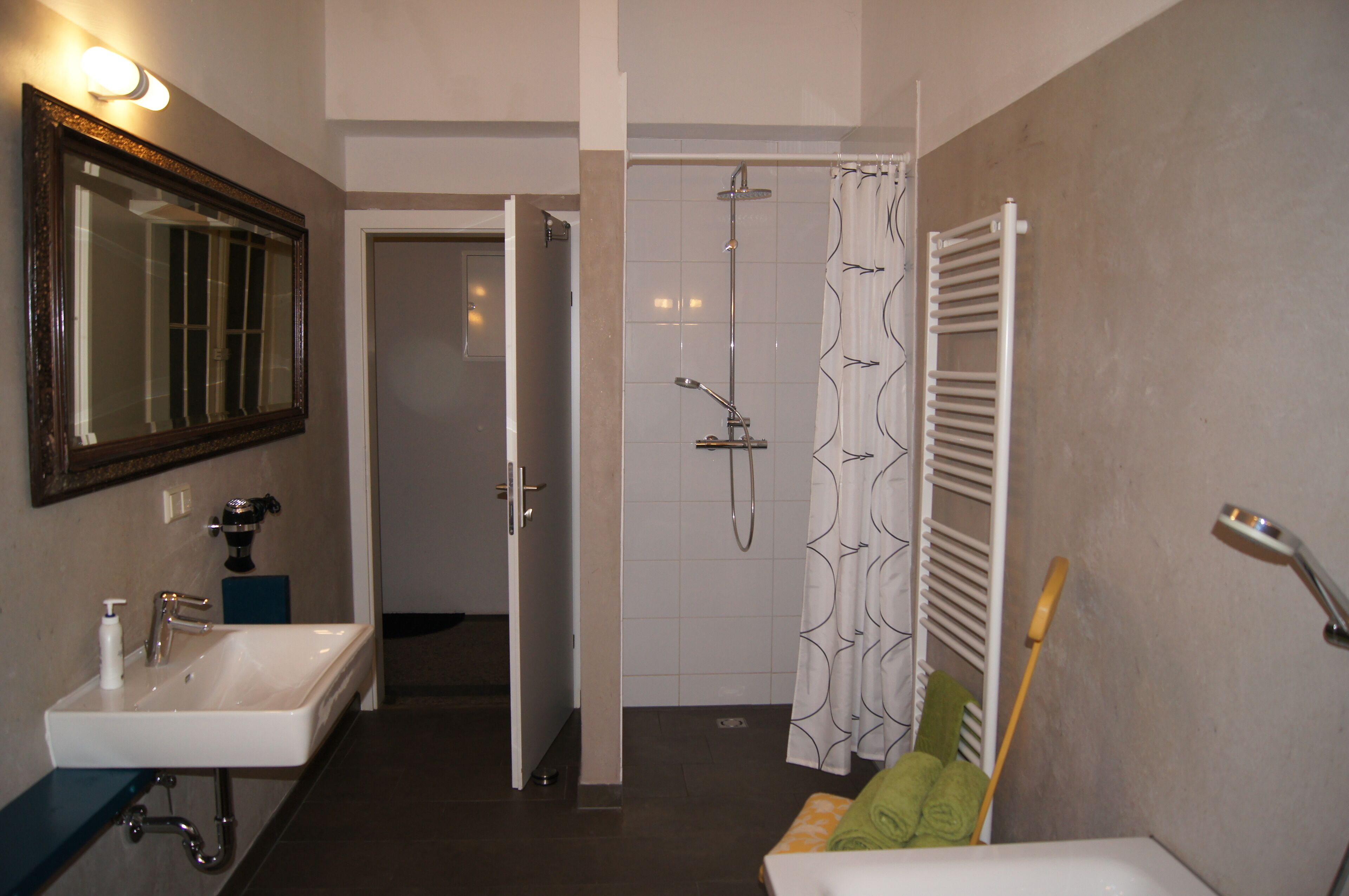 Een badkamer met een wastafel, spiegel, douche en handdoekhouder.