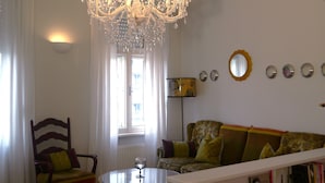 A living room with a chandelier, a sofa, a chair, a table, and a bookshelf. - Altstadthaus Cityappartements (Graz)