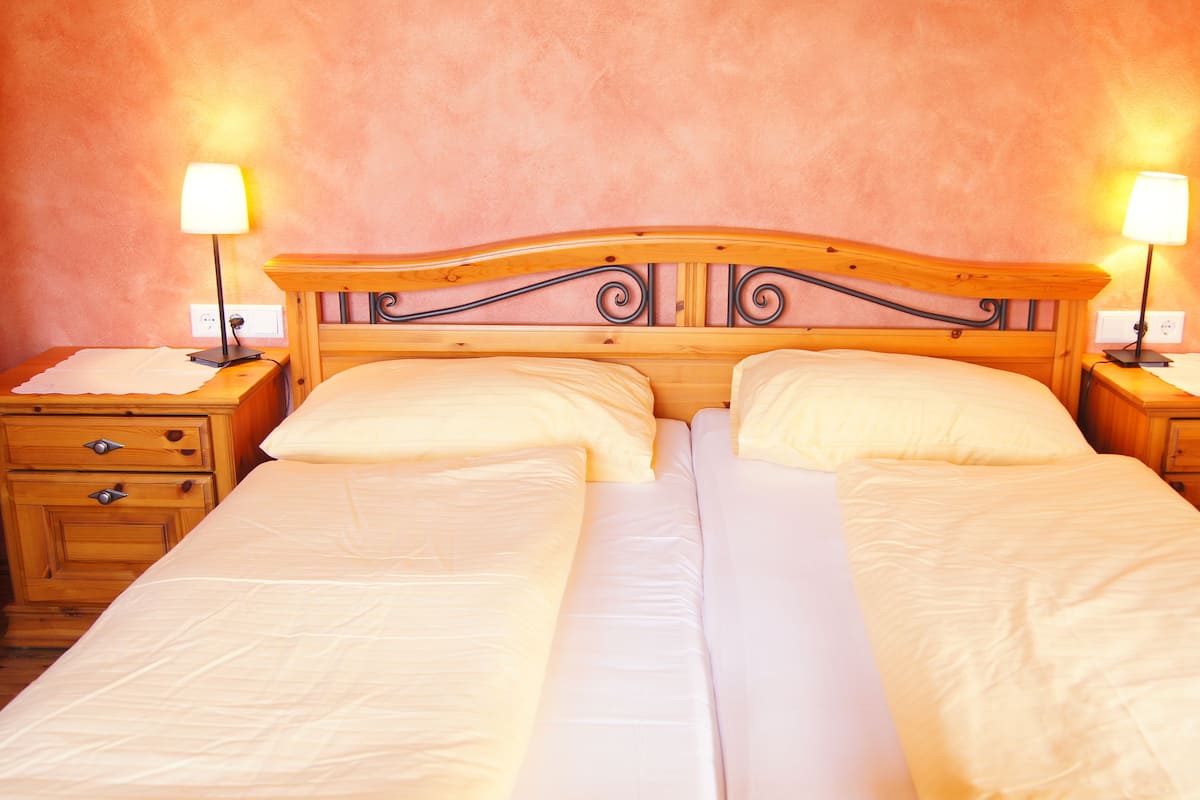 A double bed with a wooden headboard, two bedside tables with lamps, and a plain wall.