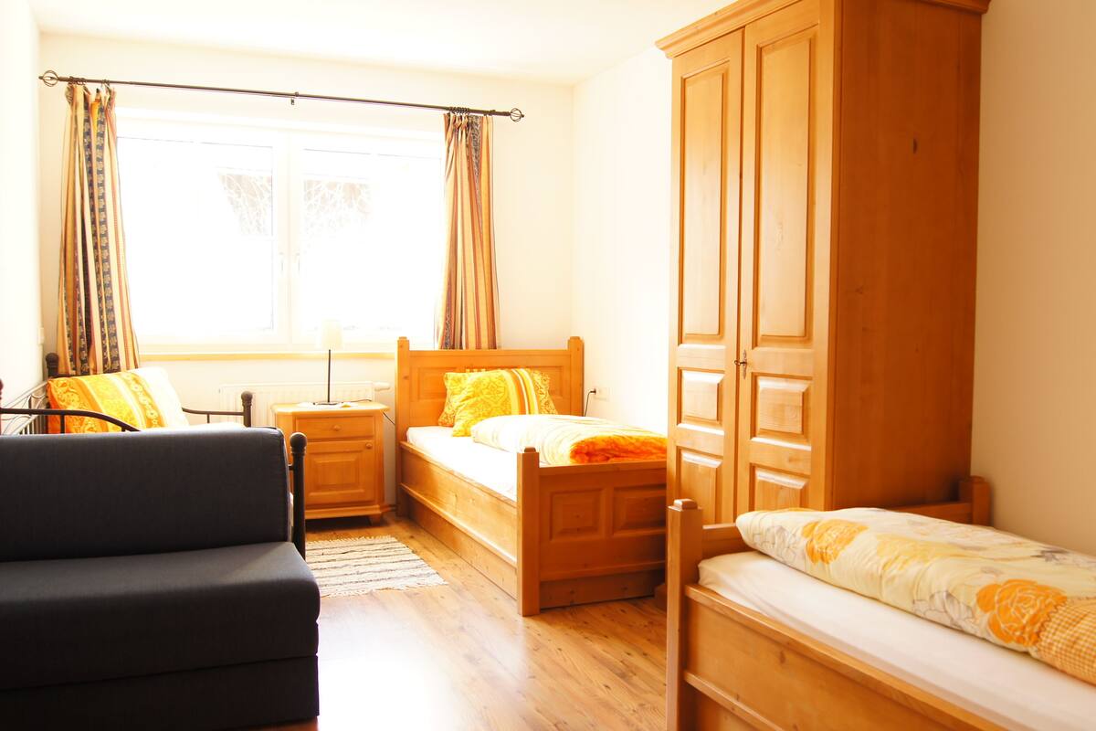 A bedroom with two wooden beds, a nightstand, a chair, and a wardrobe.