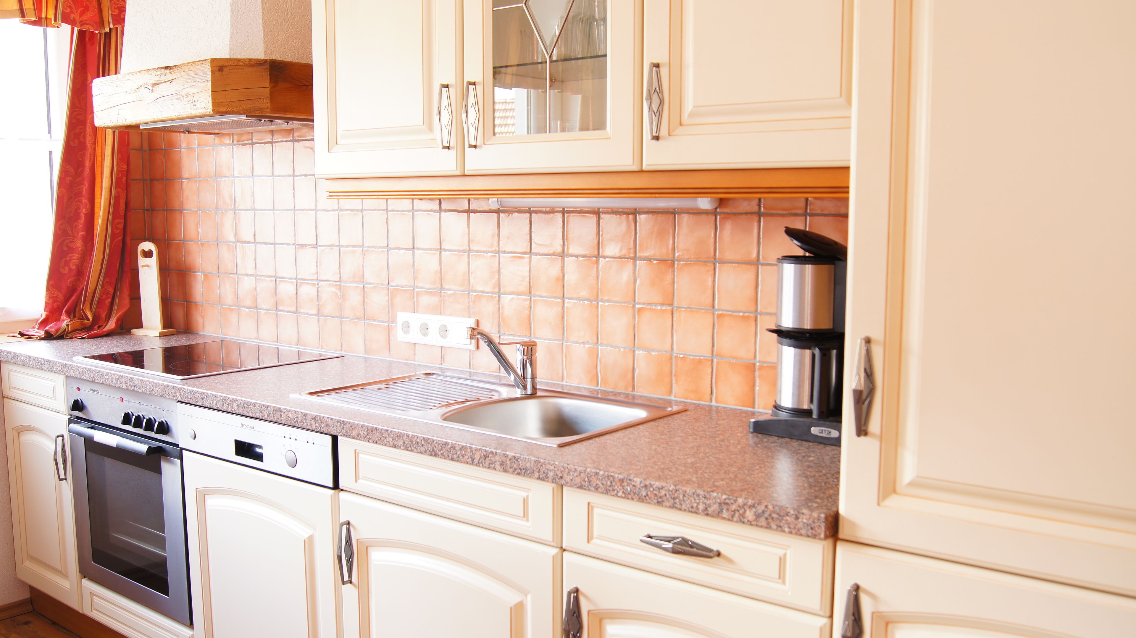 Una cocina con armarios blancos, un lavamanos de acero inoxidable, un horno empotrado y una cafetera.