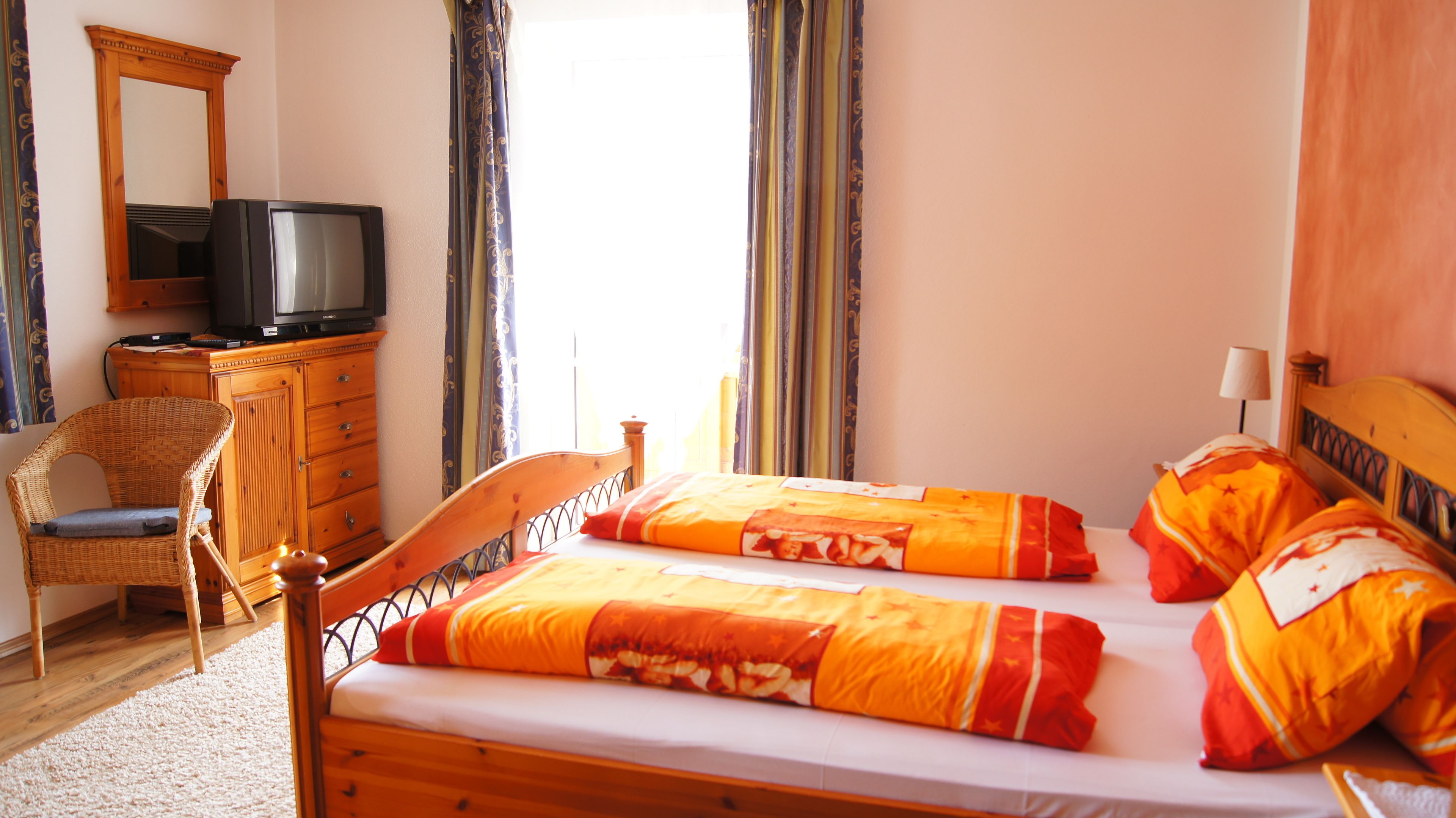 A room with a wooden bed, two pillows, a wooden dresser, a television, and a chair.