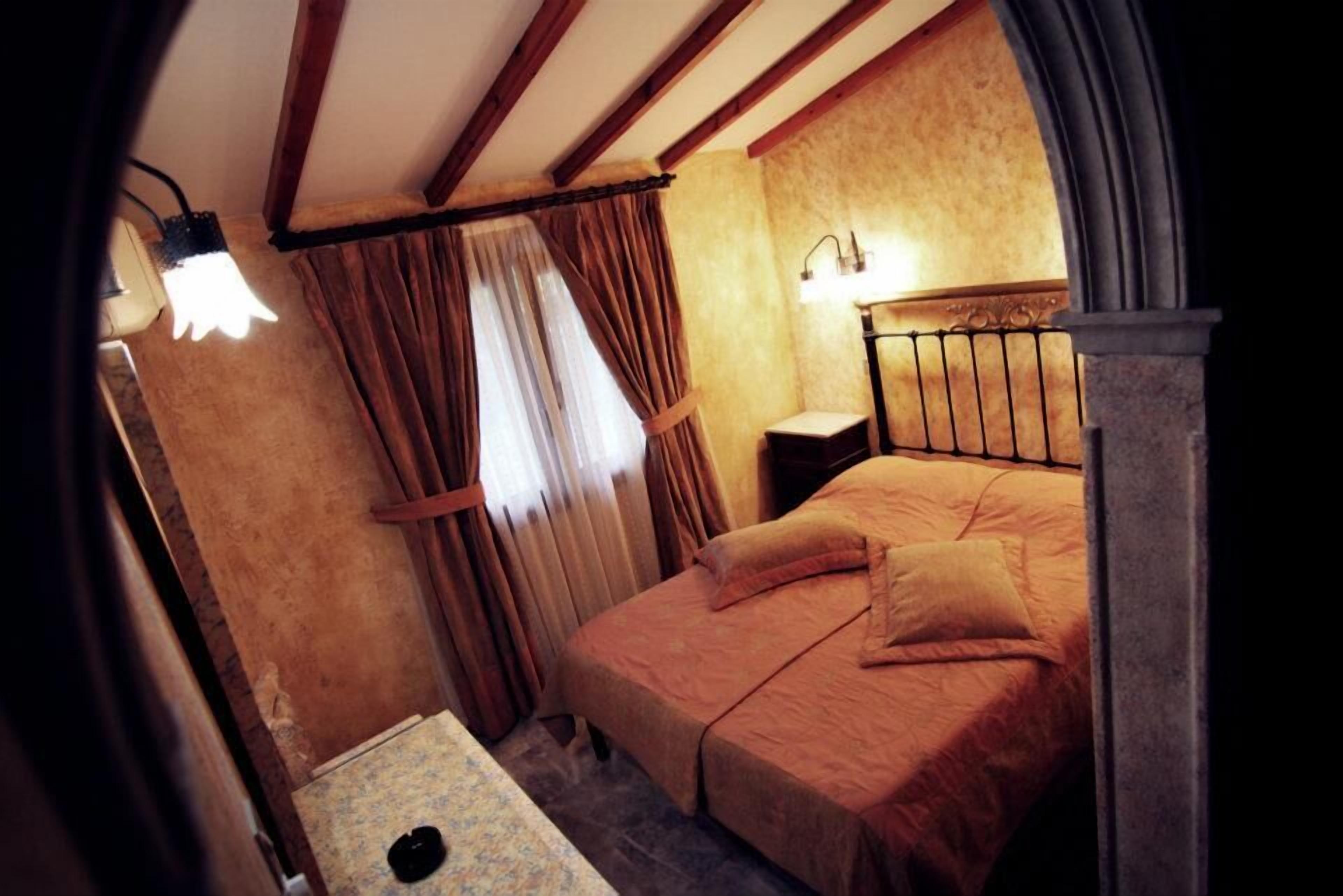 Ein Schlafzimmer mit Bett, Vorhängen, einem Nachttisch und einer Wandlampe.