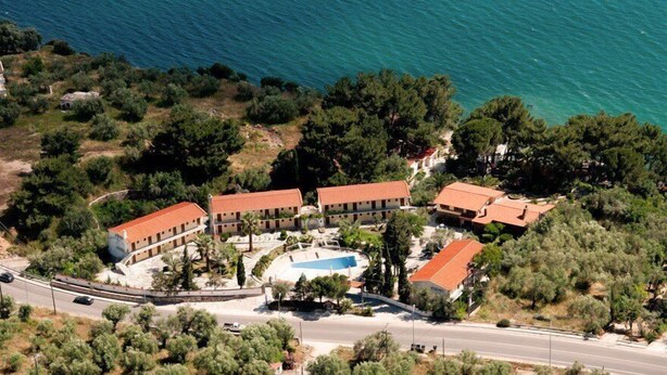 An aerial view of a coastal hotel with multiple buildings, a swimming pool, and a road. - Mytilana Village Hotel (Lesvos)
