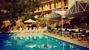 A pool area with lounge chairs and umbrellas at Mytilana Village Hotel. - Mytilana Village Hotel (Lesvos)