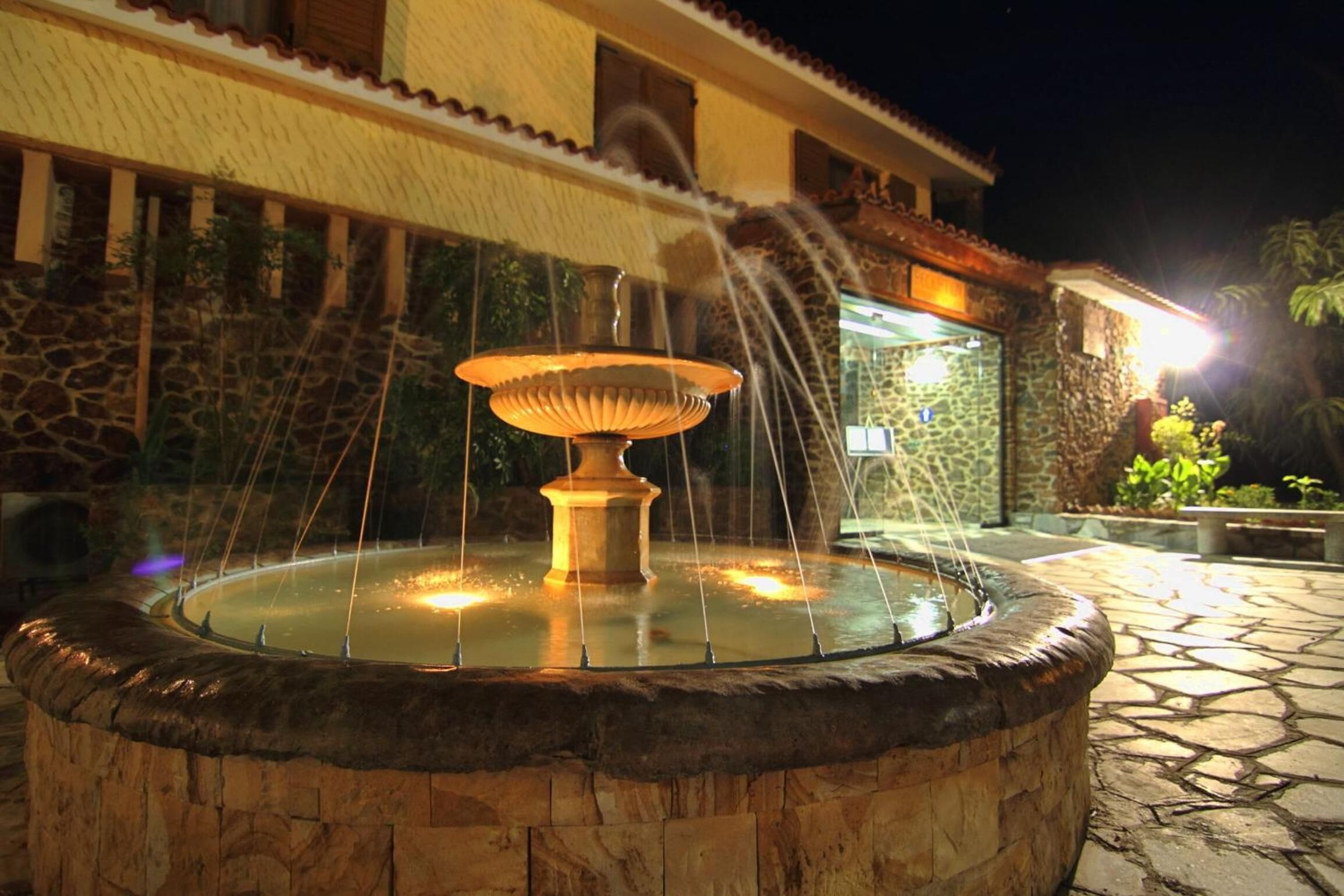 A stone fountain with water jets in a courtyard at night.