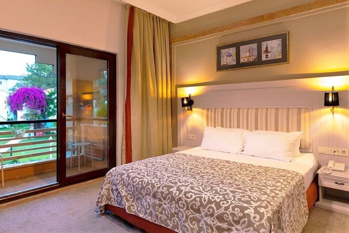 A hotel room with a large bed, a sliding glass door to a balcony, and two bedside lamps.