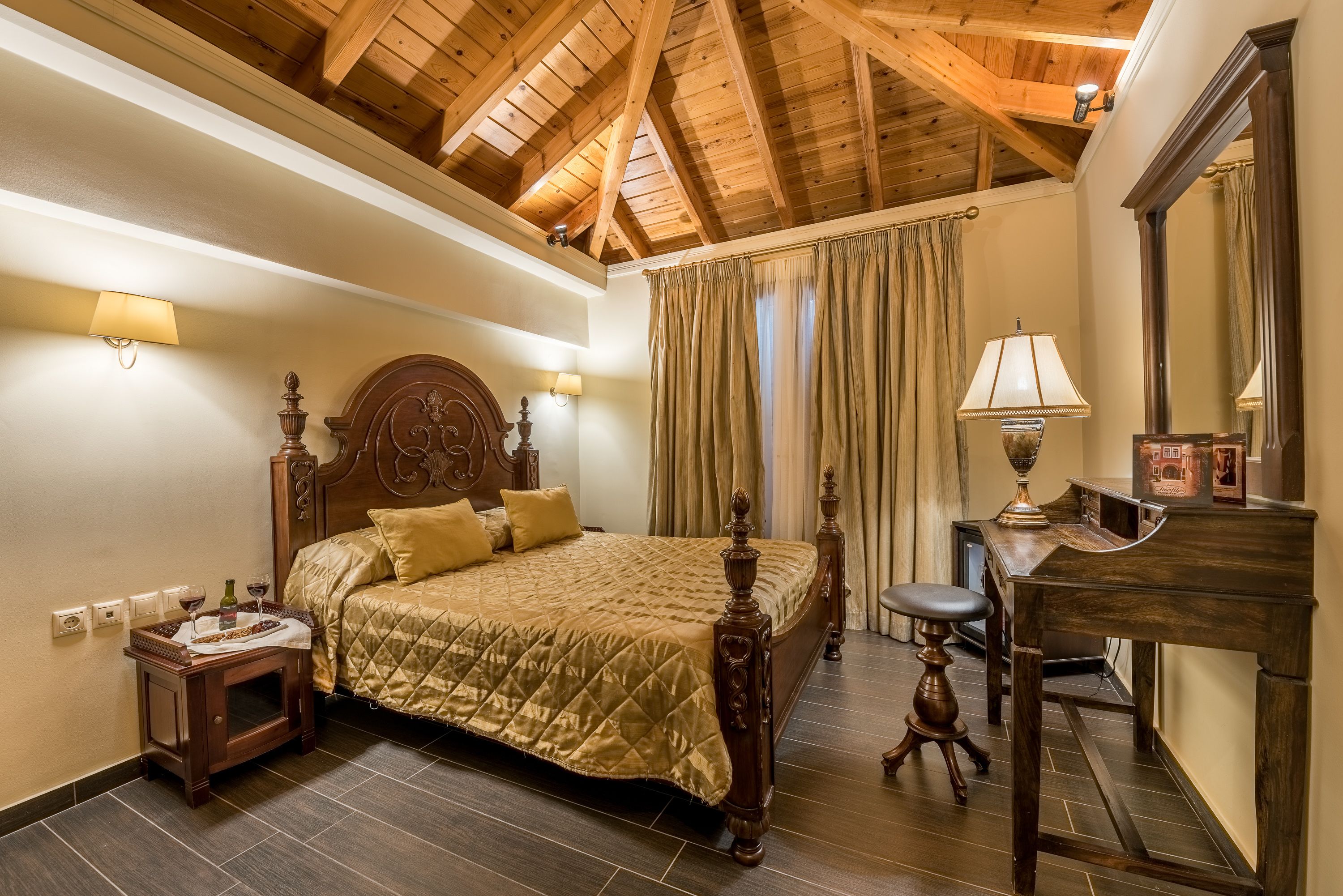 Un dormitorio con techo de madera, una cama con cabecera, una mesita de noche, un escritorio con lámpara y un espejo.