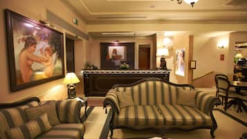 A hotel lobby with a reception desk, a sofa, a chair, and a dining area.
