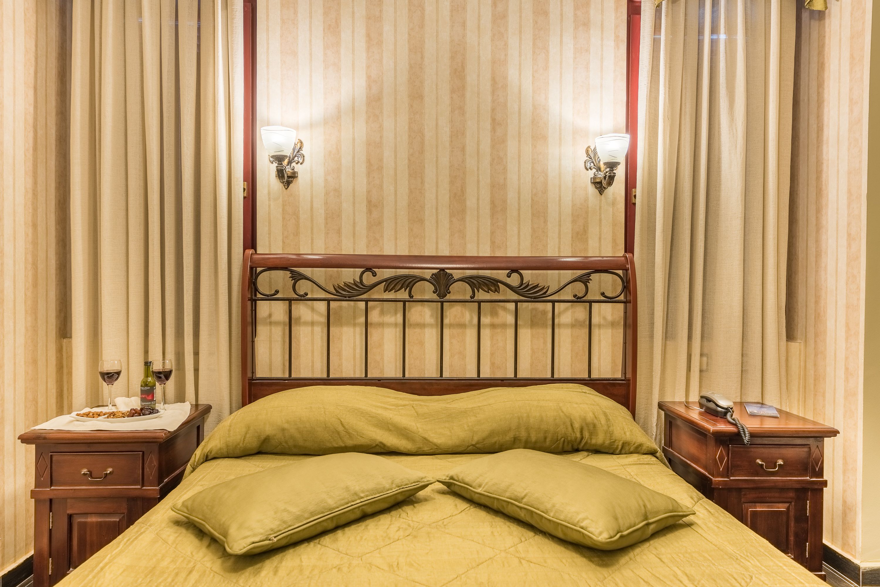 Una cama con cabecera de madera, dos mesitas de noche con lámparas y cortinas en las ventanas.