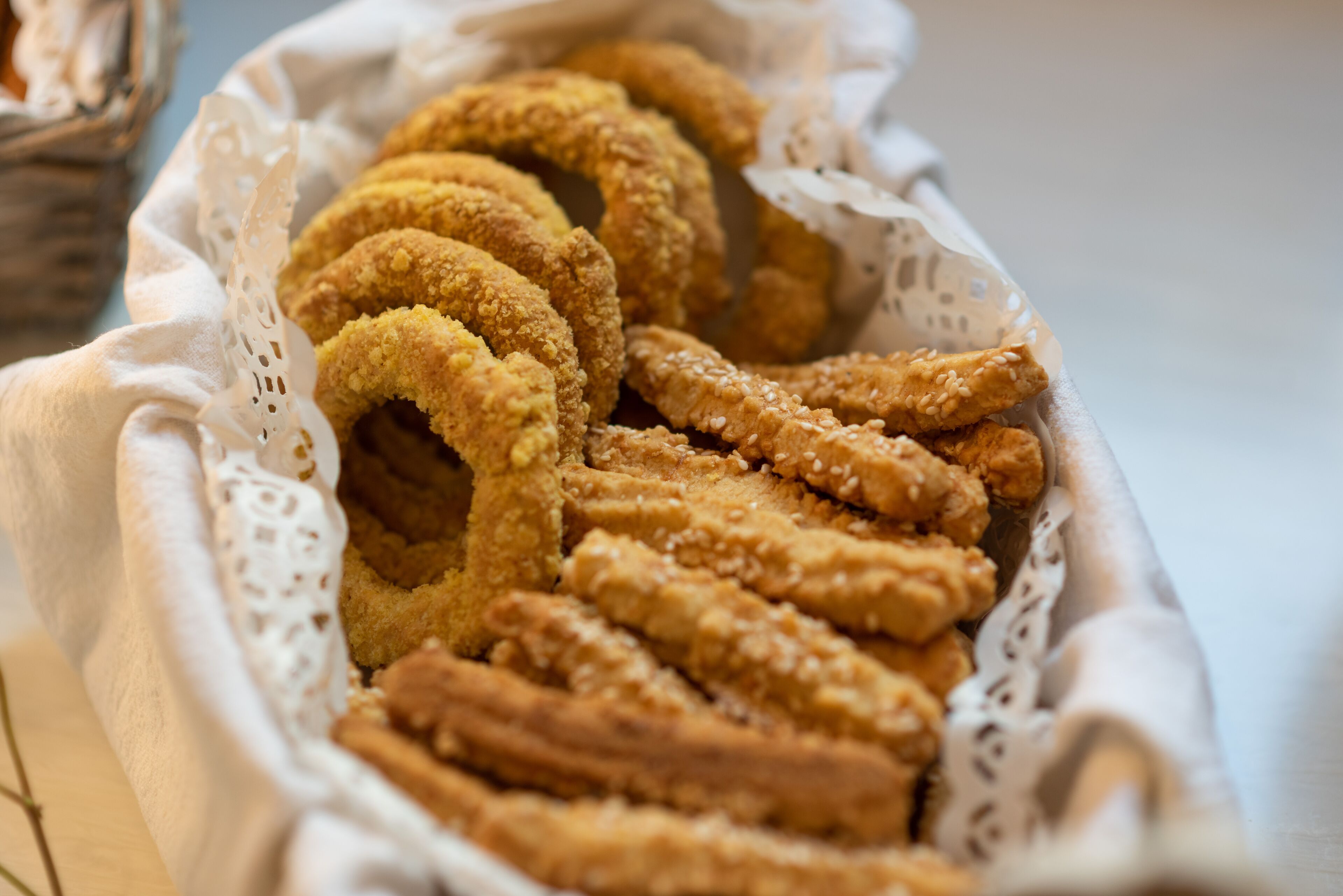 A basket of fried dough snacks, possibly churros or doughnuts, with a white lace doily.