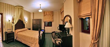 A hotel room with a bed, a desk, a chair, a television, and a lamp.