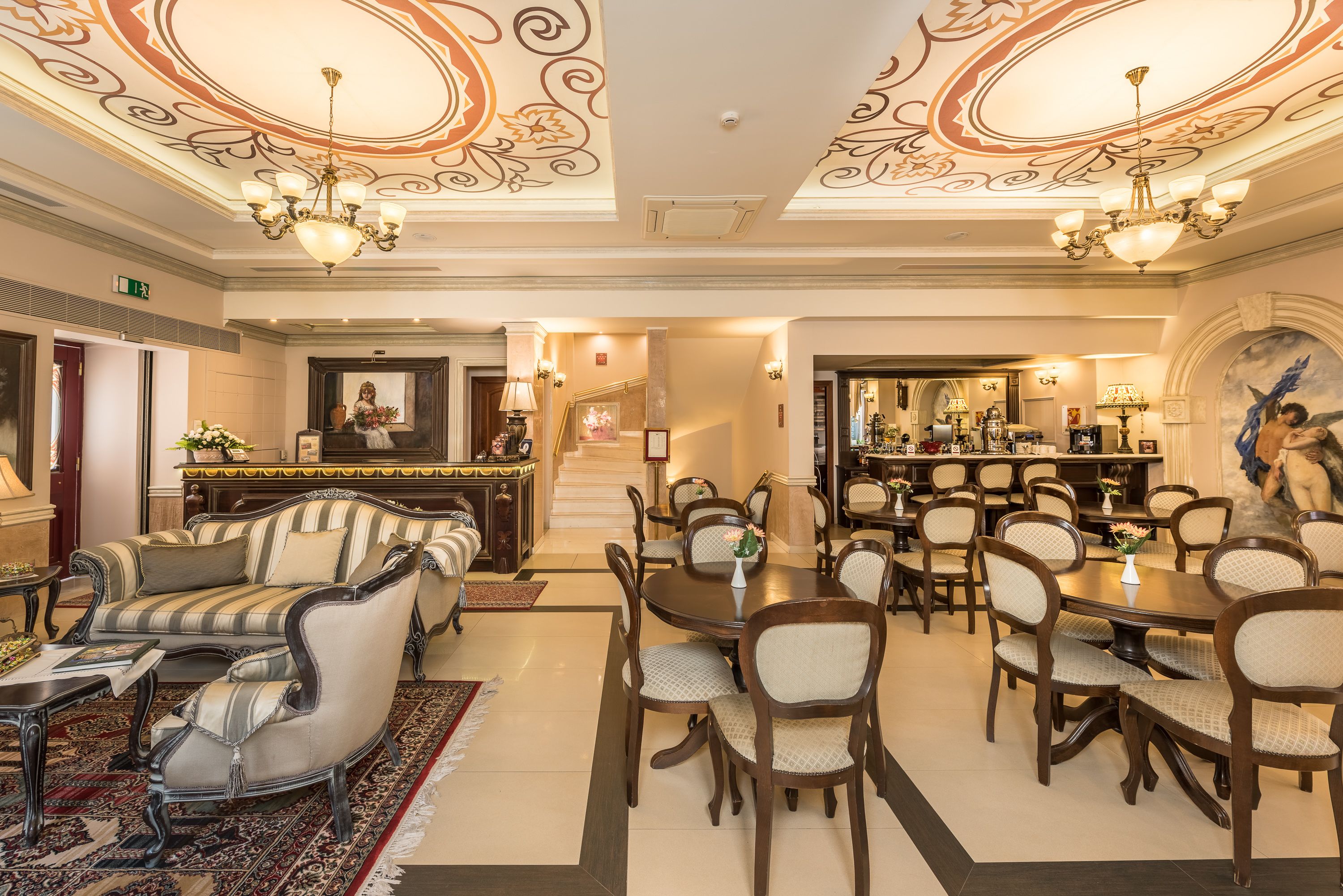 A hotel lobby with a reception desk, seating area, and a staircase leading to another floor.