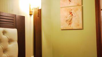 A hotel room with a tufted headboard, a bedside table with a lamp, a small wooden table, and two pieces of artwork on the wall.