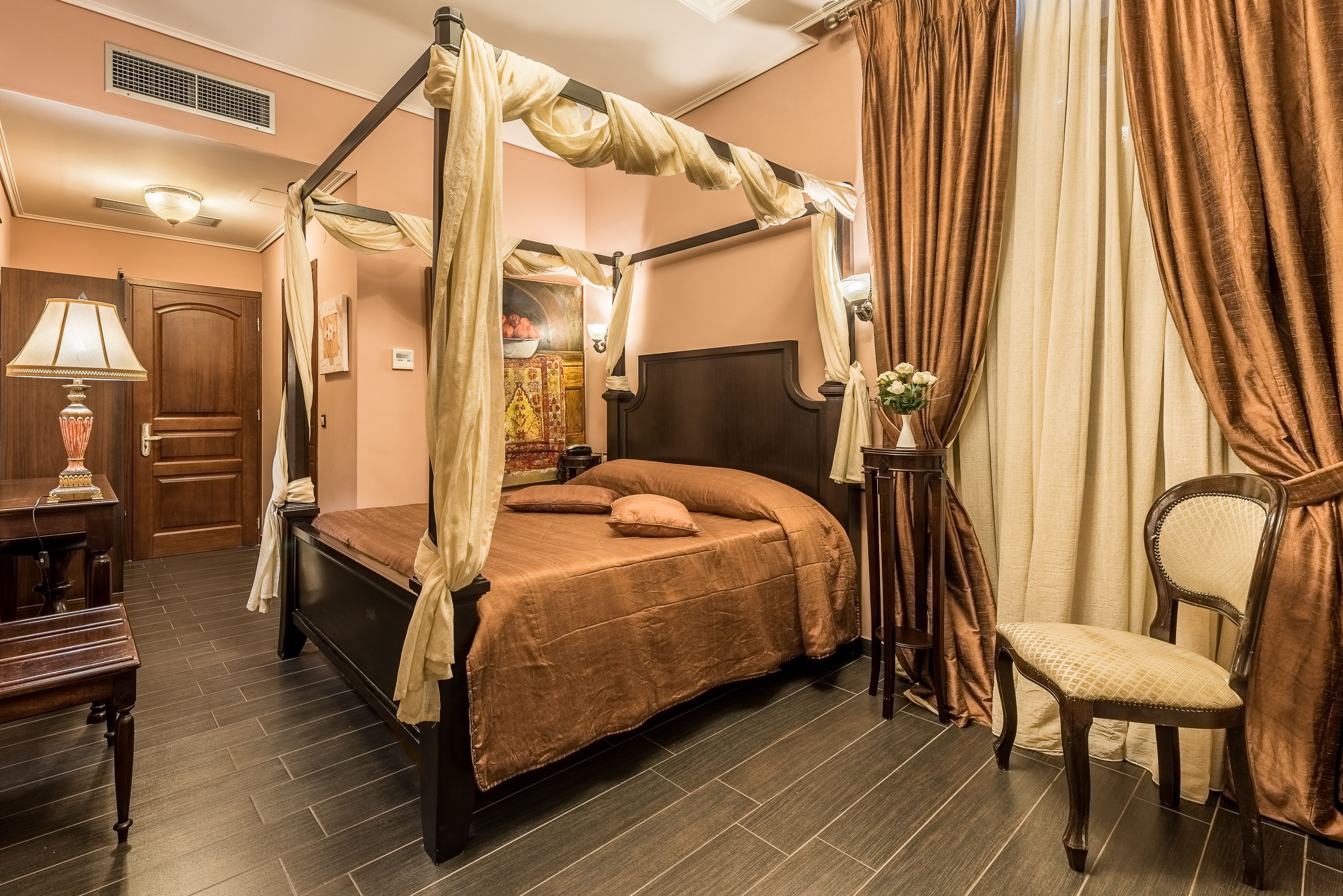A four-poster bed with a canopy, a wooden nightstand, a chair, and a desk with a lamp.