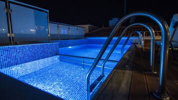 Una piscina con escalones de azulejos azules y barandillas de metal, rodeada por una terraza de madera.