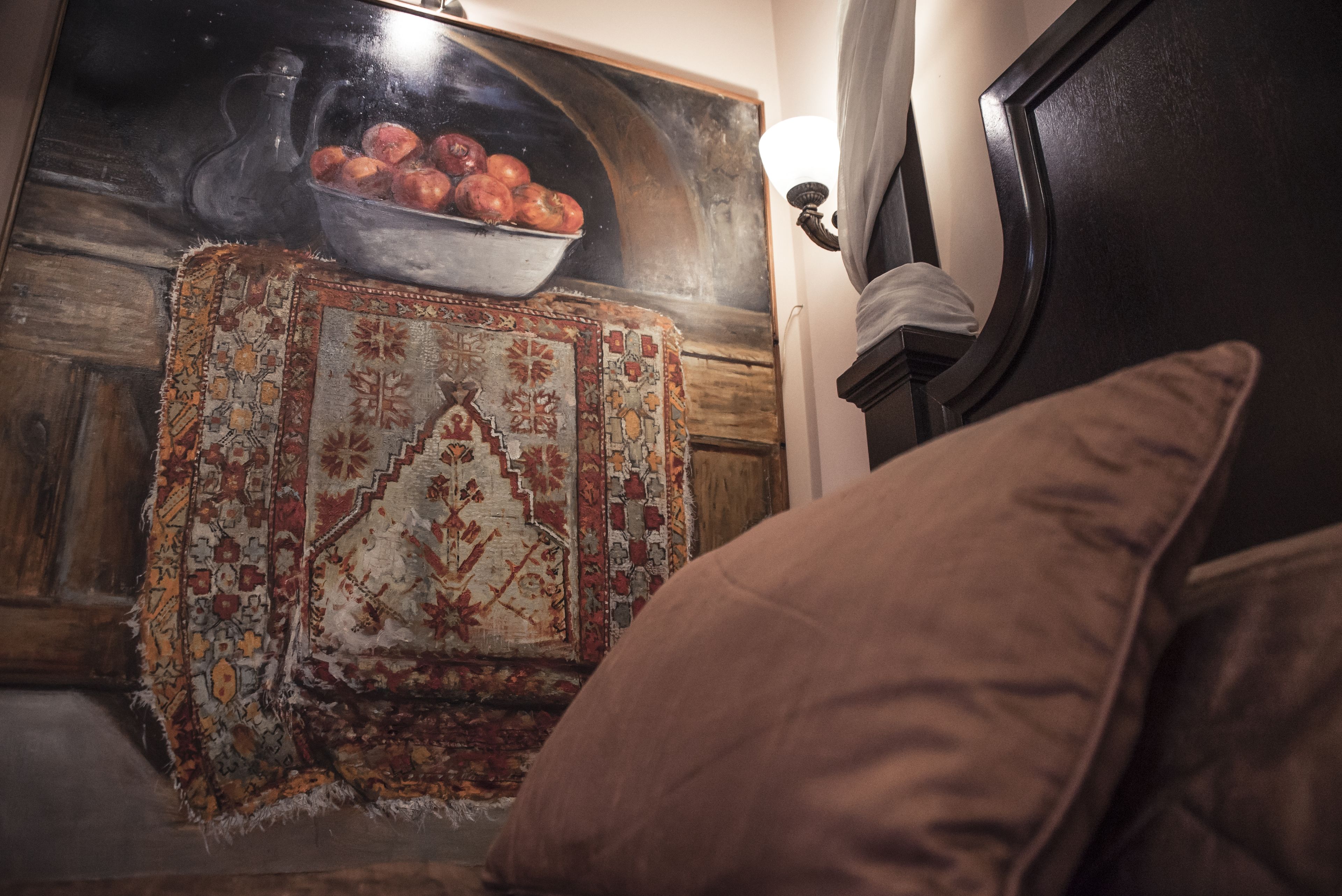 Una habitación con alfombra estampada, un tapiz decorativo y un cabecero de madera oscura.