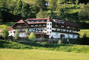 Un hotel tradicional europeo con varios balcones, una entrada destacada y un paisaje exuberante a su alrededor.