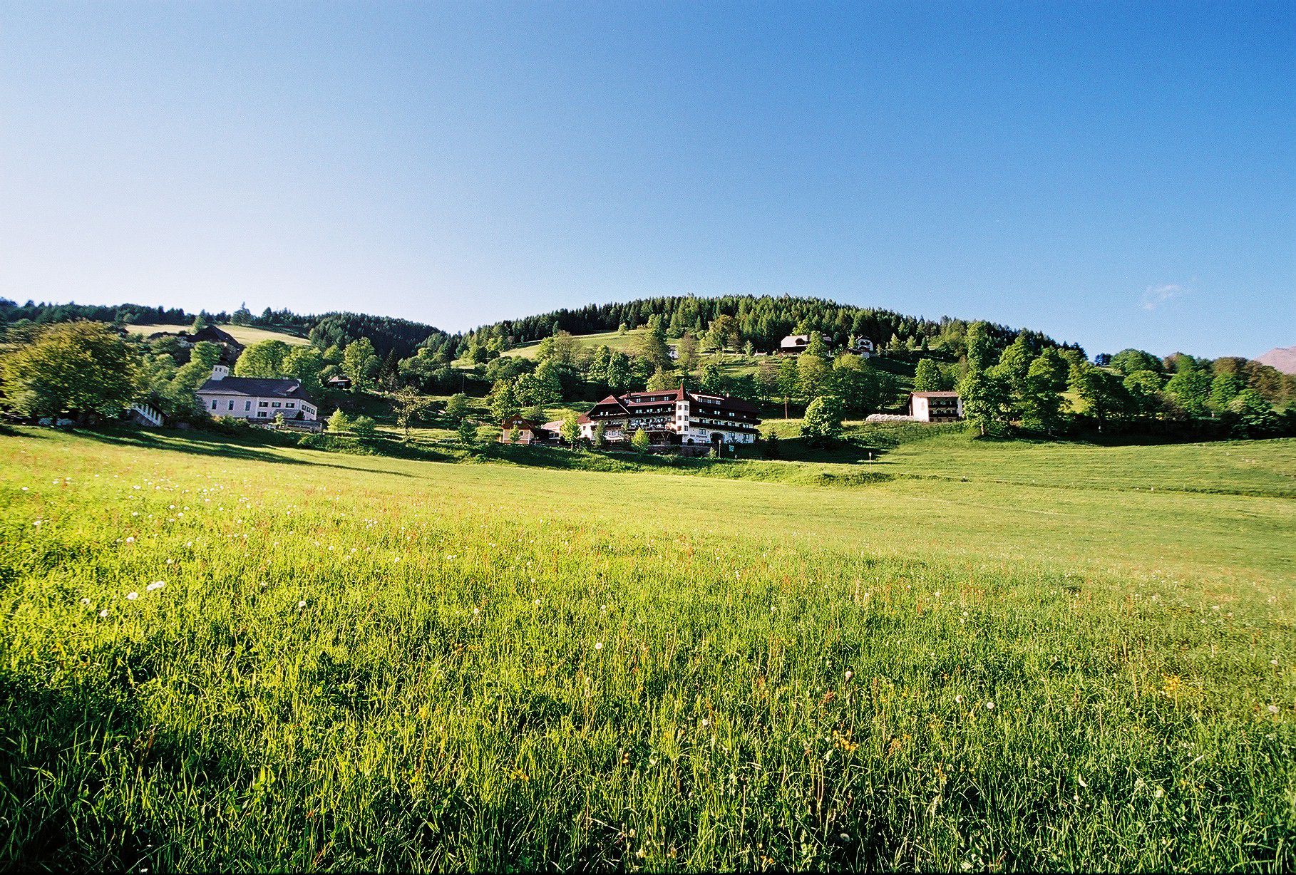 A rural landscape with a large field in the foreground and a cluster of traditional houses on a hill in the background.