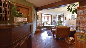 A spacious living room with a wooden coffee table, a rocking chair, and a dog. There is a bookshelf with various items and a large window providing natural light. - Hotel Stigenwirth (Krakauhintermuehlen)