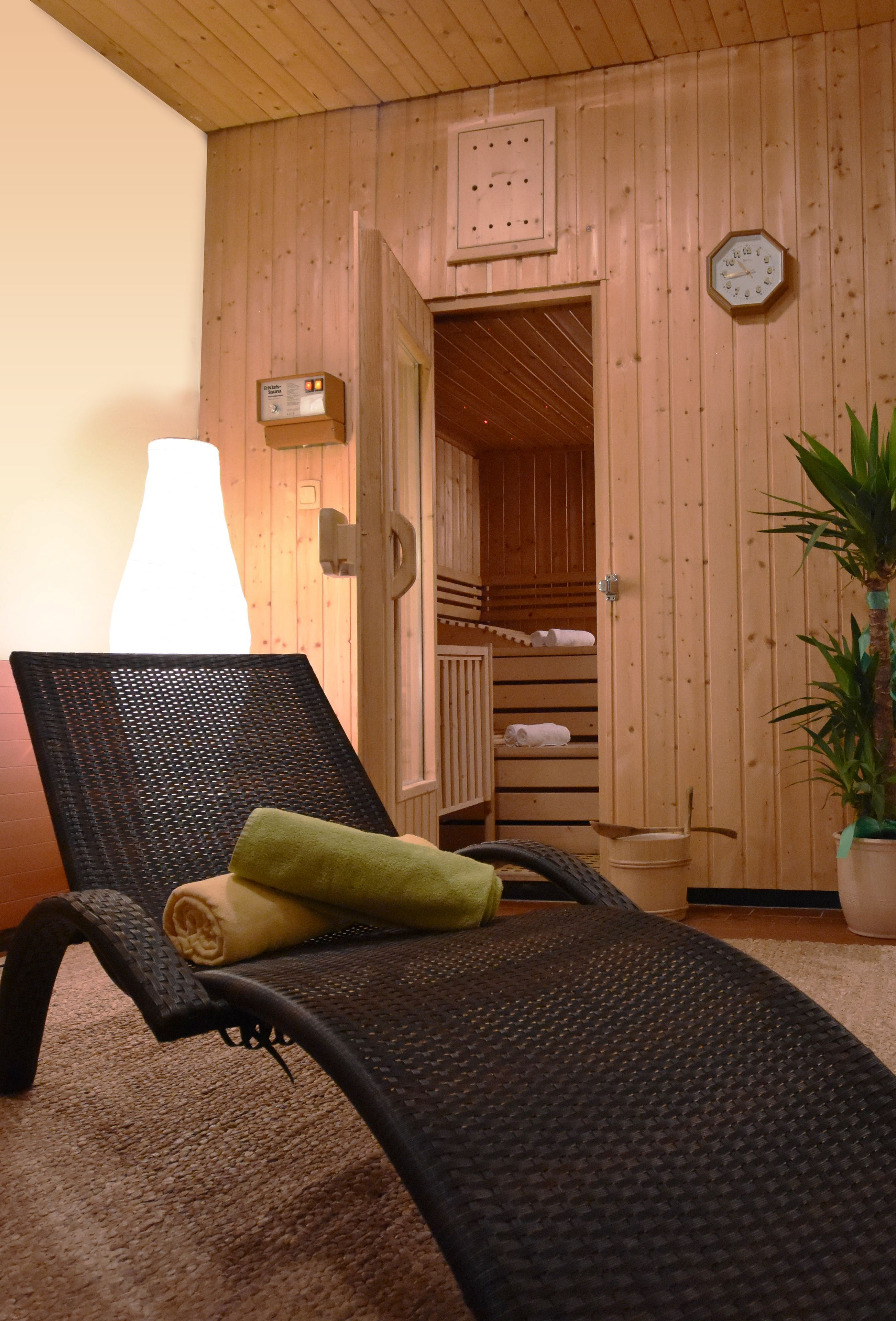 A wooden room with a black lounge chair, a towel, a potted plant, and a visible door leading to another room.