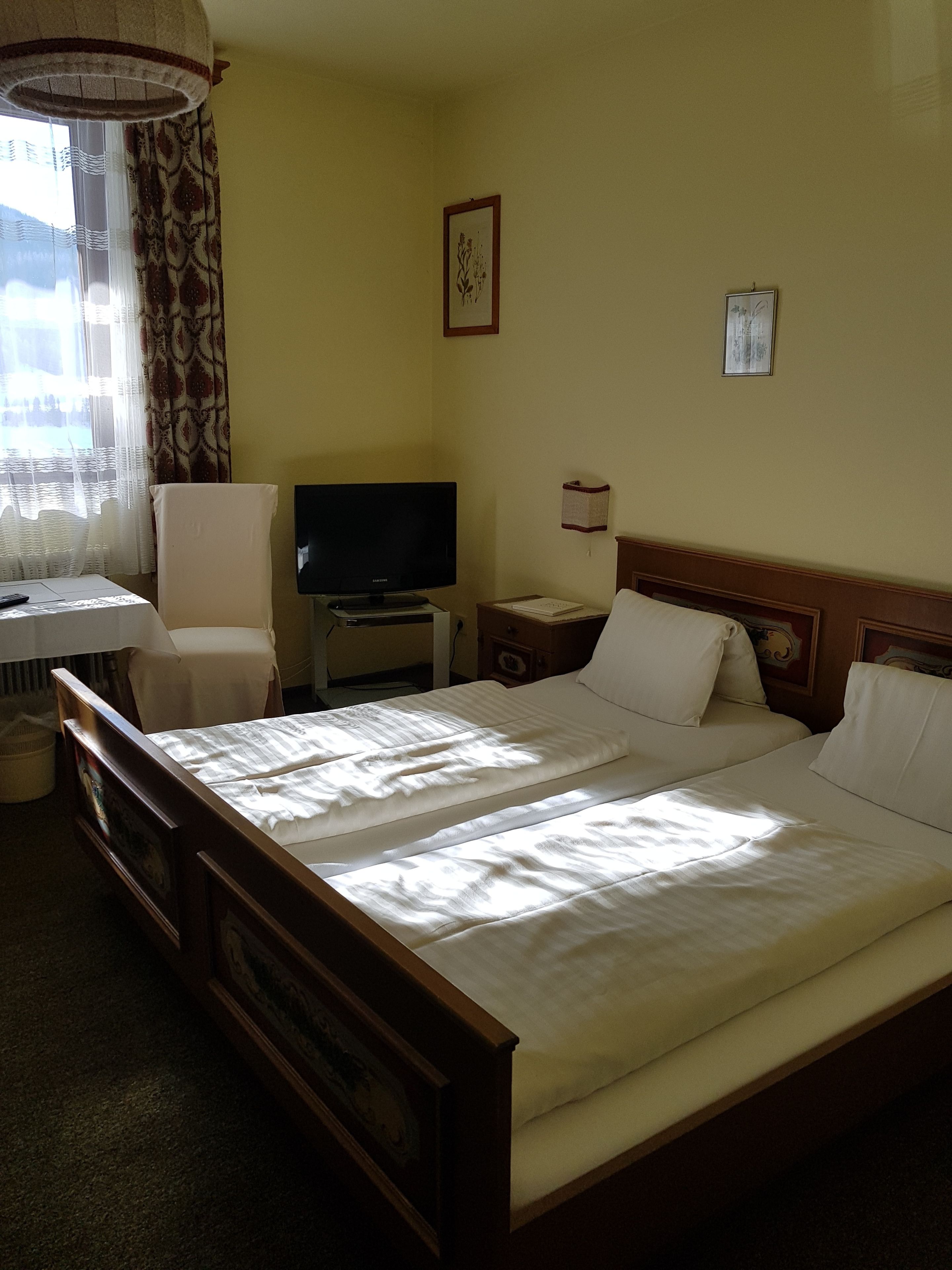 Una habitación de hotel con cama, televisión, silla, escritorio y ventana con cortinas.