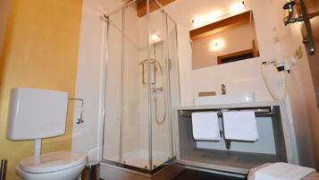 A modern bathroom with a glass-enclosed shower, a toilet, and a sink with two towels.