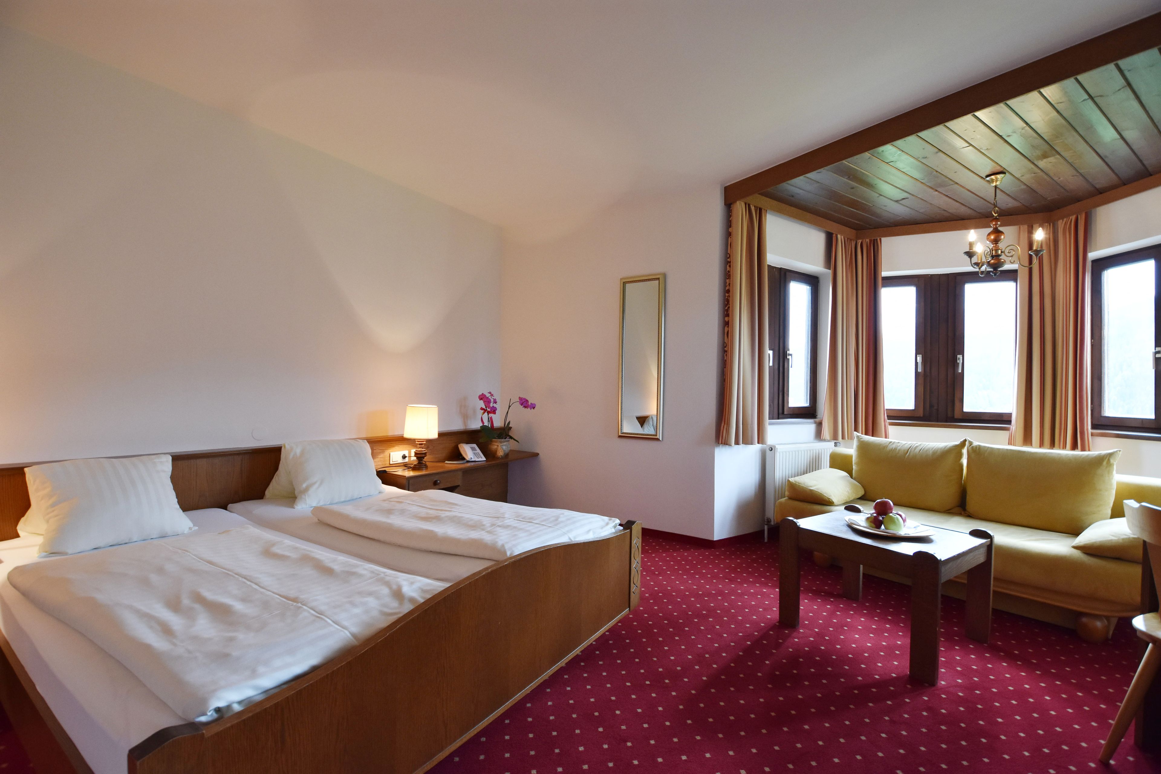 A hotel room with a large bed, a sofa, a small table, and a window with curtains.