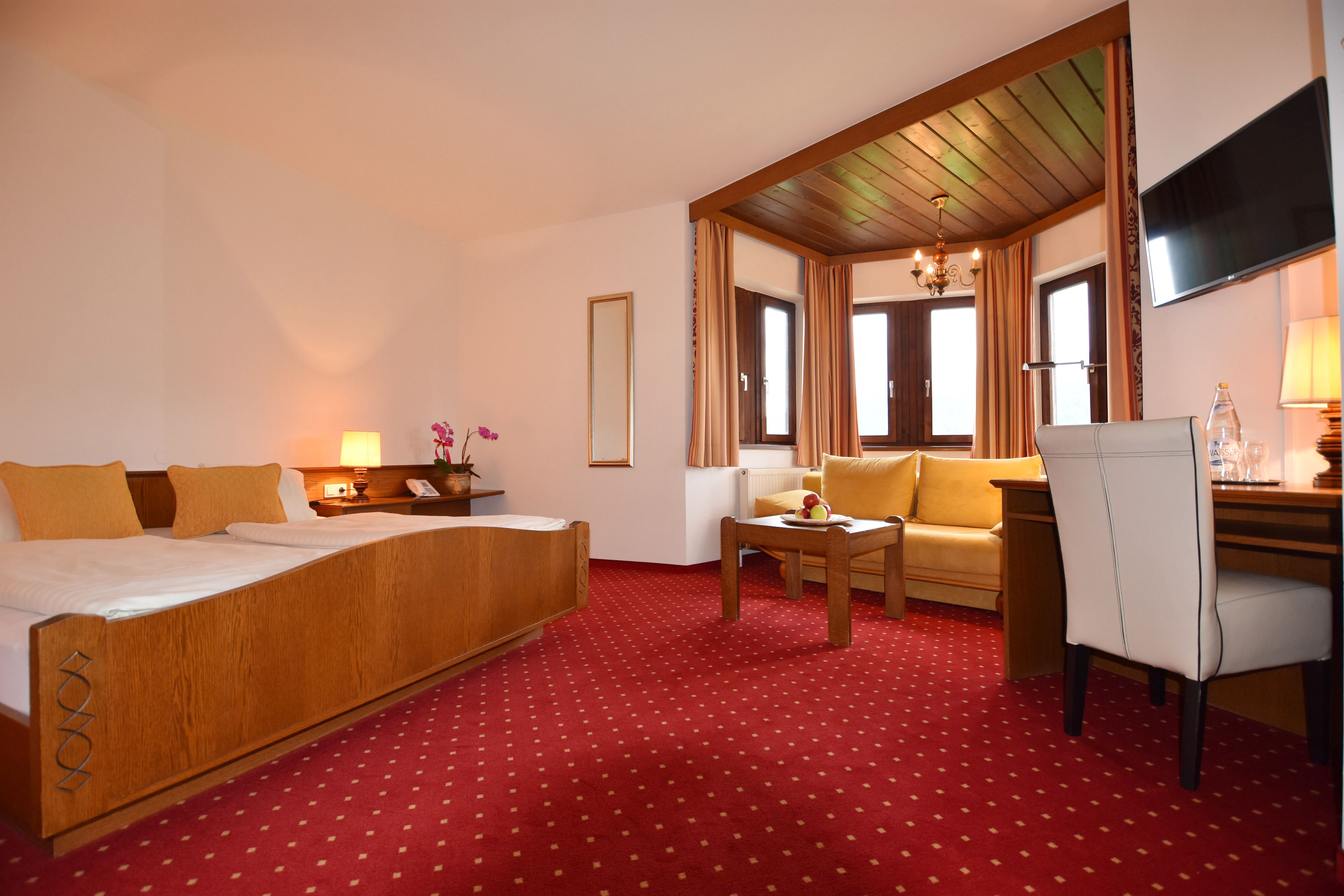 Quarto de hotel com cama, sofá, escrivaninha e televisão.