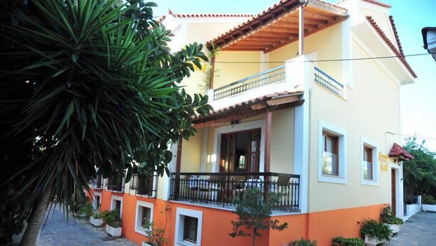 A two-story building with a balcony, potted plants, and a cobblestone pathway.