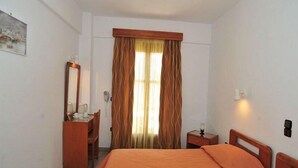 A hotel room with a bed, a desk, a chair, a mirror, and a window with curtains.