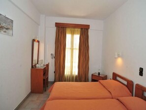 A hotel room with a bed, a desk, a chair, a mirror, and a window with curtains. - Sama (Samos)