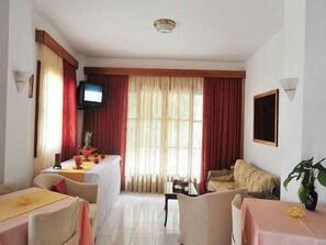 A hotel room with a dining area, a television, a sofa, and a plant. - Sama (Samos)