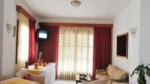 A hotel room with a dining area, a television, a sofa, and a plant.