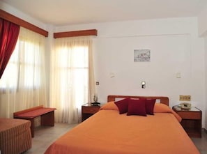 Ein Hotelzimmer mit einem großen Bett, einem Nachttisch, einem Sessel, Vorhängen und einem kleinen Tisch.