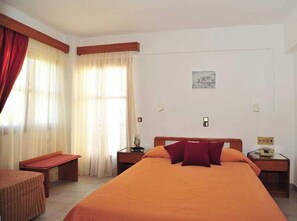 Une chambre d’hôtel avec un grand lit, deux tables de chevet, une chaise et une fenêtre avec des rideaux.