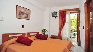 A double bed with a red and orange bedspread, a small bedside table with a plant, a TV mounted on the wall, and a balcony with a red curtain. - Sama (Samos)