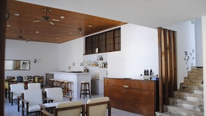 Ein geräumiger Essbereich mit Holztischen und -stühlen, eine Bar mit Barhocker und eine Treppe, die in einen oberen Bereich führt.