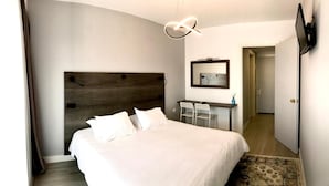 Ein Hotelzimmer mit einem großen Bett, einem Schreibtisch mit zwei Stühlen, einem an der Wand montierten Fernseher und einer Tür zu einem weiteren Raum.