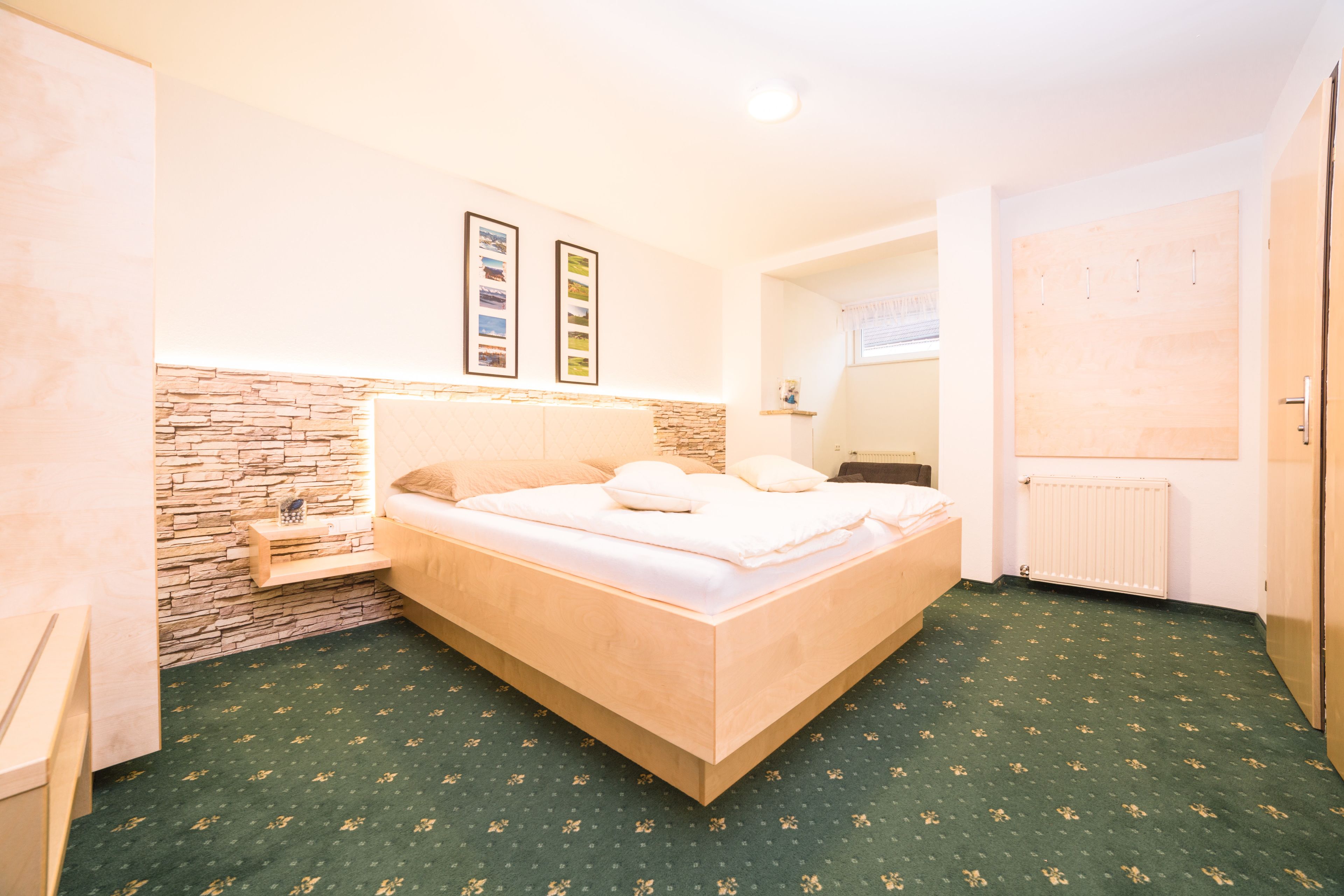 A bedroom with a bed, a stone accent wall, a small shelf, a radiator, and a door.