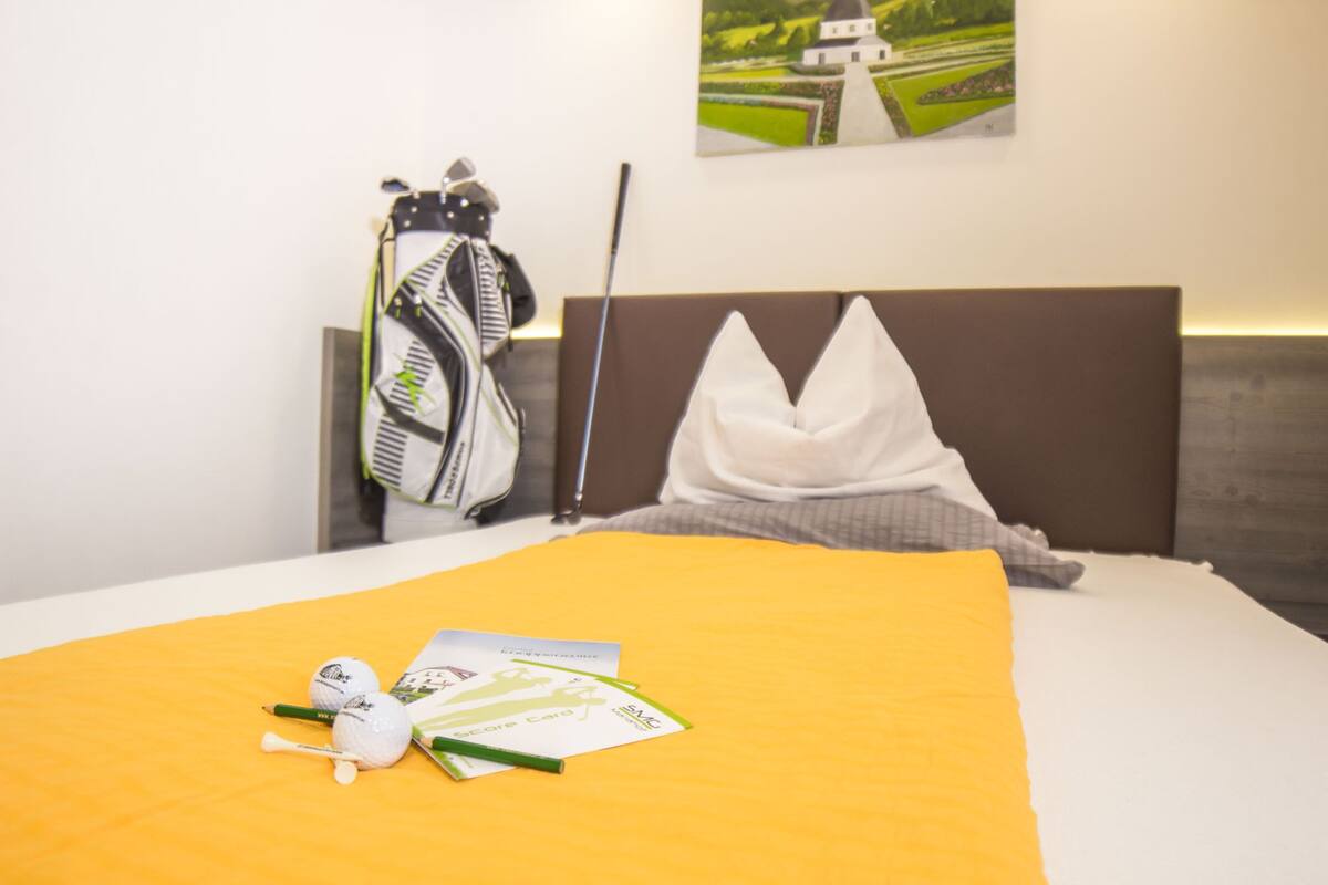 Habitación de hotel con una cama bien hecha, un bolso de golf y un palo de golf apoyado en la pared.