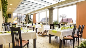 Un restaurante con varias mesas dispuestas para comer, ventanas amplias y vistas al exterior.