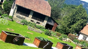 Un granero rústico con techo inclinado, rodeado de vegetación exuberante y montañas al fondo.